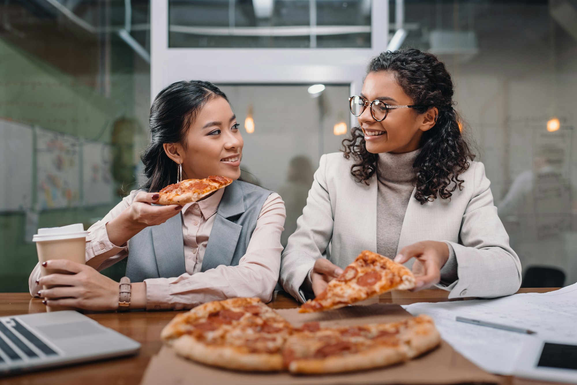 multiethnic businesswomen having lunch in office, eating pizza